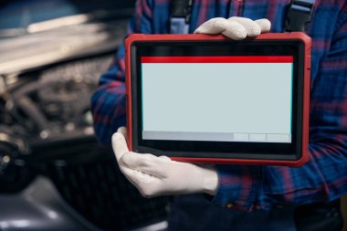 Koruyucu kostümlü tamirci otomobilde oturuyor ve tableti tutarak çalışmaya hazır.