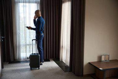 Gündüz vakti otel odasında cep telefonuyla konuşan pasaport sahibi Afro-Amerikan erkek girişimcinin yan görüntüsü. İş gezisi, tatil ve seyahat kavramı