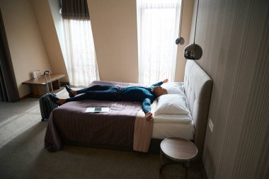 Gündüz vakti otel odasında yatakta uyuyan Afrikalı Amerikalı erkek girişimcinin yan görüntüsü. İş gezisi, dinlenme, tatil ve seyahat kavramı