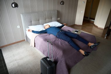 Yorgun Afrikalı Amerikalı iş adamı gündüzleri otel odasında yatakta uyuyor. İş gezisi, dinlenme, tatil ve seyahat kavramı