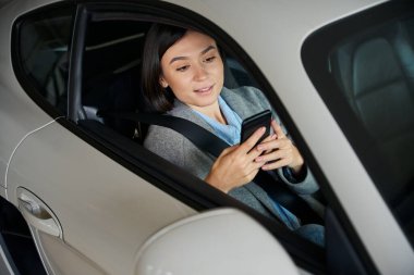 Emniyet kemeri takan güzel bir kadın, cep telefonu tutuyor, koca ya da erkek arkadaşını beklerken mesajları kontrol ediyor ve mesaj atıyor.