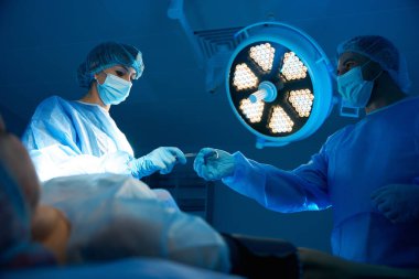 Profesyonel doktorlar ve asistanlar ameliyathanede tıbbi aletler kullanarak lamba altında ameliyat yapıyorlar.