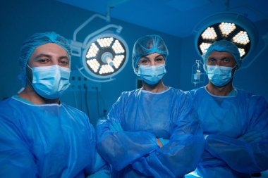 Hastane tiyatrosunda ameliyat yapan profesyonel cerrahlar steril üniformalar ve tıbbi maskeler takıyor.