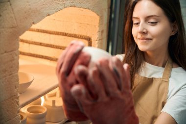 Eldivenli eğlenceli kadın çömlekçi çömlek atölyesinde seramik ürünler üretiyor.