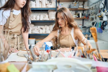 Önlük giymiş el işi kadın çömlekçiler çömlek atölyesinde kil levhalar hazırlıyorlar.