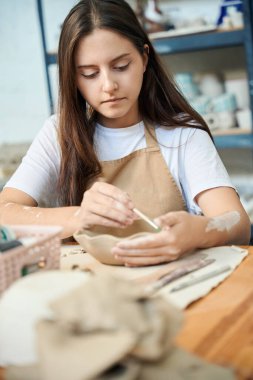 Esmer kadın seramik stüdyoda boya fırçasıyla kil kase boyuyor.