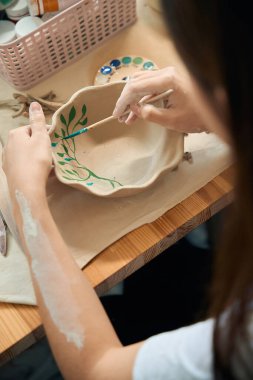 Kadın çömlekçi elleri çömlek atölyesinde fırçayla el yapımı seramik kâse boyuyor.