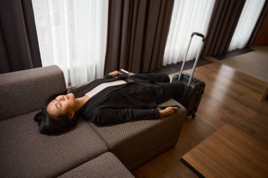 Otel odasındaki kanepede uzanmış ve dinlenen gözleri kapalı mutlu bayan. Üst Manzara. Seyahat, iş konsepti