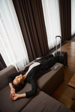 Güzel bir kadın otel odasında kolları kanepede uzanıyor. Kadının yanında bir bavul var. Seyahat, iş konsepti