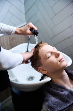 Modern berber dükkanında gözleri kapalı yakışıklı müşterinin kafasını yıkayan yetenekli bir berber.