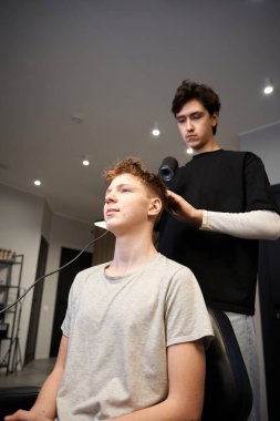Modern berber dükkanında saç kurutma makinesi ve tarak ile genç bir müşterinin saçını kurutan konsantre bir berber.