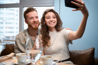 Birbirine aşık mutlu çift, restoranda bir masada oturmuş, kendi fotoğrafını çekiyor.