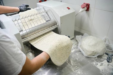 İşçi çarşaf makinesine bir parça hamur koyar, bir kadın metal bir yüzey üzerinde çalışır.