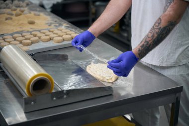 Yarı bitmiş ürün atölyesinin çalışanı Khachapuri paketliyor, bir rulo streç film kullanıyor.