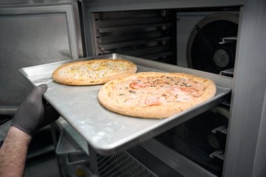 Yarı bitmiş ürün atölyesinin çalışanı, dondurucuya pizza ile metal bir levha gönderiyor, modern ekipman kullanıyor.