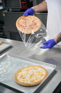 Üniformalı aşçı şeffaf bir çantada pizza paketleri, kolunda dövme olan bir adam.