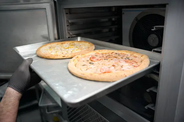 stock image Employee of the semi-finished products workshop sends a metal sheet with pizza to the freezer, he uses modern equipment