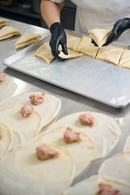 İşçi, metal bir çarşafta donmak için kıymalı krep ve koruyucu eldiven giyen bir kadın yerleştiriyor.