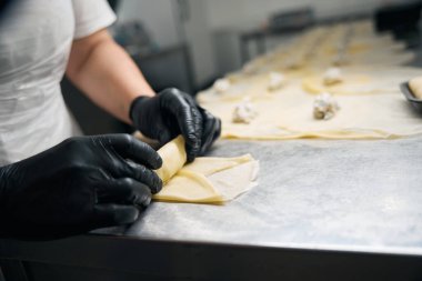 Kadın işçi müşteriye teslim etmek için börek hazırlar, büyük bir masada çalışır.