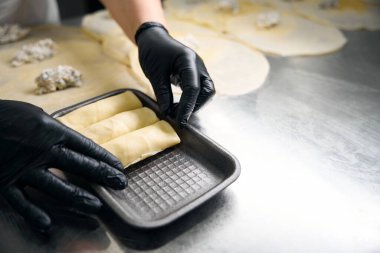 Kadın işçi bir müşteriye teslim etmek için börek paketliyor, büyük bir masada çalışıyor.