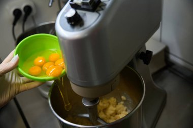 Kadın pastacı, hamur hamuruyla mutfak karışımına bir sürü yumurta ekliyor. Orta yavaş, Avrupa mutfağında karışımı yeniyor.