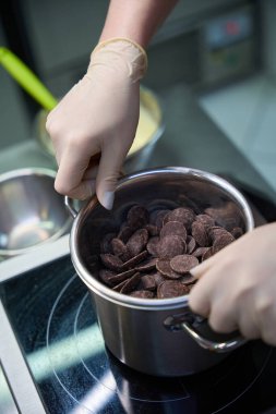 Kadın pastacı bir kase çikolatayı kaynayan suyun üzerine koyuyor. Çikolatayı eritip ganache veya krema yapıyor.