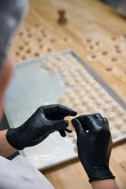 Kadın büyük ahşap bir masada hamur tatlısı yapıyor. Bitmiş ürünleri metal bir levhaya koyuyor.