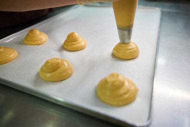 Pastanenin yakın çekim işçisi hamur işlerini hamur işinden pasta kağıdına dönüştürüyor, daireler oluşturuyor, profesyonel mutfakta profiterol pişiriyor.