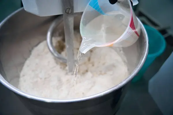 stock image Cook pours water into a container with flour, an employee uses a dough kneading machine