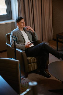 Elinde cep telefonu olan düşünceli bir işadamı otel odasındaki kahve masasında oturuyor.