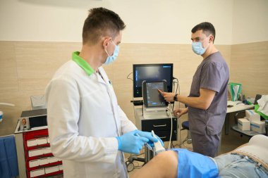 Doktor, meslektaşı tarafından yönetilen ultrason rehberliğinde hastanın dizkapağına şırınga iğnesi yerleştiriyor.