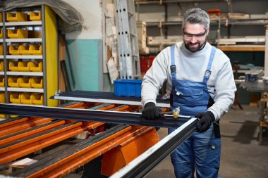 Alüminyum profilden yapılmış bir pencere çerçevesi ile çalışıyor. Koruyucu eldiven ve gözlük kullanıyor.