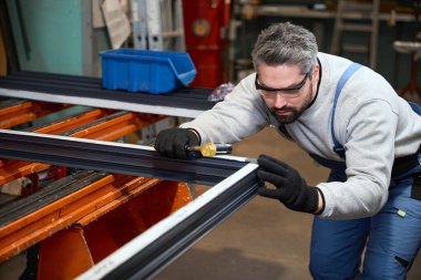 Profesyonel olarak alüminyum profilden yapılmış bir pencere çerçevesiyle çalışıyor. Koruyucu eldiven ve gözlük kullanıyor.