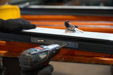 İşçi pencere profiliyle çalışmak için matkap kullanıyor, atölyede çalışan bir adam.