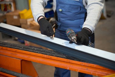 Atölyede matkapla gezen bir adam koruyucu eldiven takıyor.