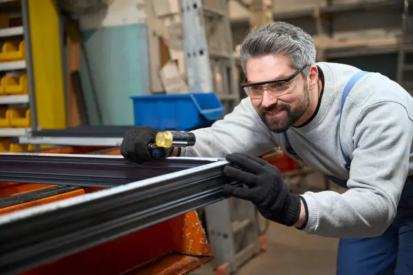 Stock image Bearded employee works with a window frame made of aluminum profile, he uses protective gloves and glasses