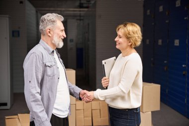 Erkek, yük arabasının yanında duruyor. Deponun yanındaki kutular istiflenmiş ve kadınlara el sıkışıyor.