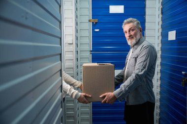 Depoda elinde karikatür kutusu olan bir adam depodaki işçilere kargo veriyor.