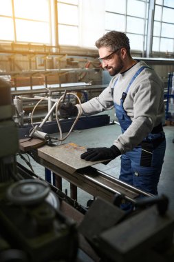 Orta yaşlı bir adam metal parçalı modern bir makinede çalışıyor, güvenlik gözlüğü kullanıyor.