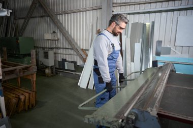 Bir yapım atölyesinin çalışanı alüminyum bir profil oluşturur, modern ekipman üzerinde çalışır.