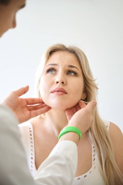 KBB doktoru, fiziksel muayene sırasında korkmuş kadın hastanın tükürük bezlerini elle muayene ediyor.