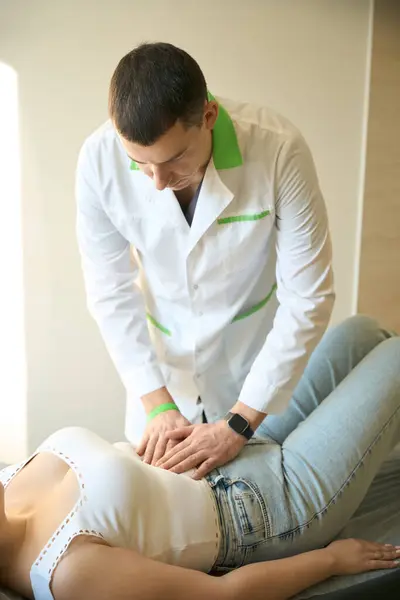 stock image Young doctor palpating abdomen of female patient lying in supine position on exam table