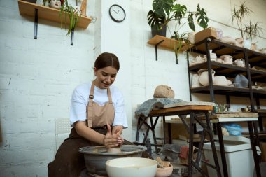 Çömlekçi çarkında seramik demlik yapan gülümseyen genç kadın. El işi seramik çömlek üretimi