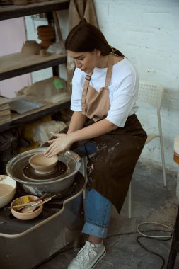 Önlüklü kadın atölyedeki dairede toprak kasesi yapıyor. El işi seramik çömlek üretimi