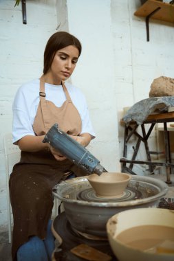 Bir atölyede çalışan çömlekçi kadın, çömlekçi çarkı üzerinde çalışıyor. El işi seramik çömlek üretimi