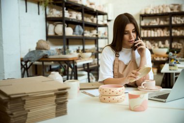 Seramik atölyesinde dizüstü bilgisayarla arama yapan genç bayan, internetten sipariş verin. Küçük işletme kavramı