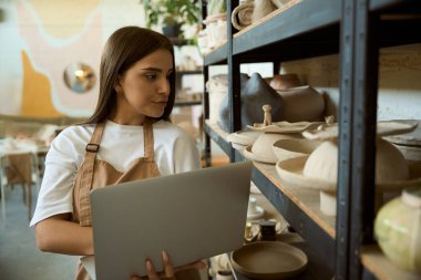 Sanat stüdyosunda dizüstü bilgisayar kullanan genç bir bayan çömlekçi. Küçük işletme kavramı