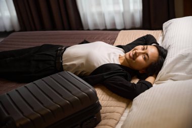 Gülümseyen Asyalı kadın, gülümsüyor ve gülümsüyor. Deneyimli avukat profesyonel konferansa geldi. Lüks bir otelde, yurtdışında iş gezisinde, bavuluyla yakınlarda yatıyordu.