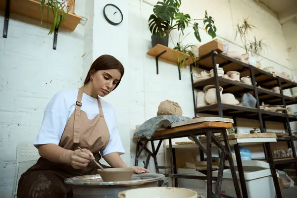 Önlüklü genç bir kadın atölyede çömlekçi çarkında kase yapıyor. El işi seramik çömlek üretimi
