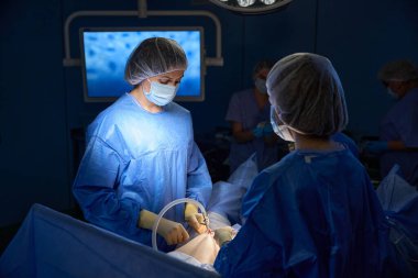 Koruyucu üniformalı profesyonel doktorlardan oluşan bir ekip ameliyathanede ameliyat yapıyor.